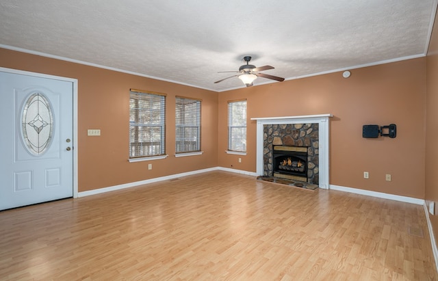 unfurnished living room featuring light wood-type flooring, ornamental molding, a textured ceiling, ceiling fan, and a fireplace