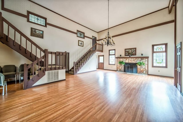 living room featuring a high ceiling, a stone fireplace, a healthy amount of sunlight, and wood-type flooring