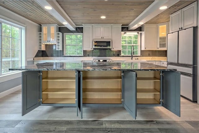 kitchen with wooden ceiling, dark stone counters, stainless steel appliances, and a wealth of natural light