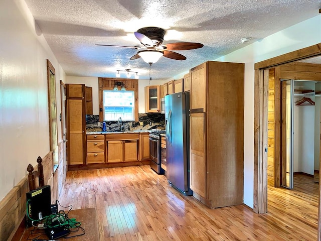 kitchen featuring light wood-style flooring, brown cabinetry, stainless steel appliances, a sink, and a textured ceiling