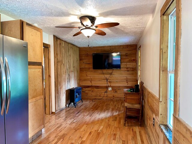 living room with wood walls, a textured ceiling, light wood-type flooring, and a ceiling fan