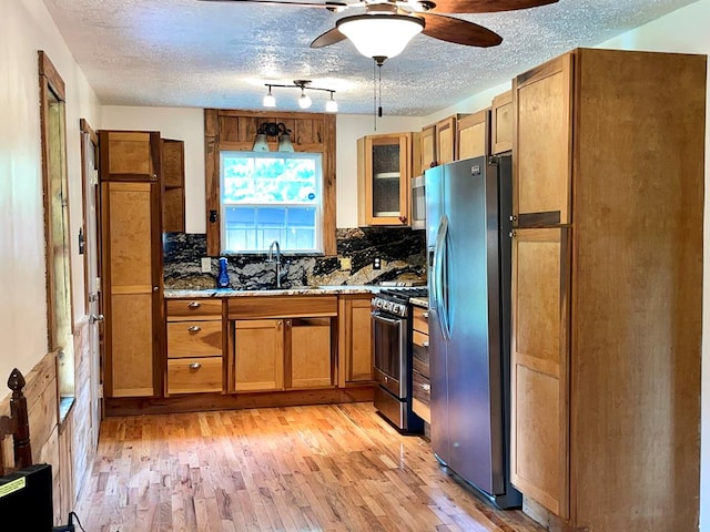 kitchen featuring light hardwood / wood-style floors, light stone countertops, stainless steel appliances, ceiling fan, and sink