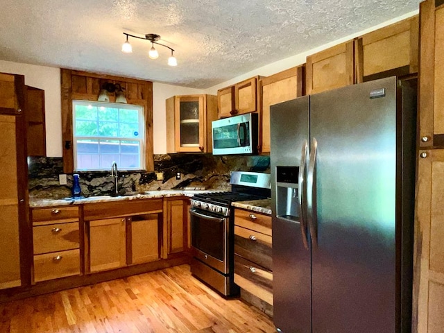 kitchen with appliances with stainless steel finishes, decorative backsplash, brown cabinets, and light wood-type flooring