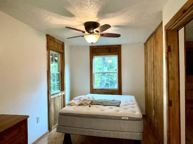 bedroom with a textured ceiling, ceiling fan, and light wood-style floors