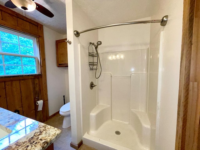 bathroom with a textured ceiling, baseboards, walk in shower, toilet, and a ceiling fan