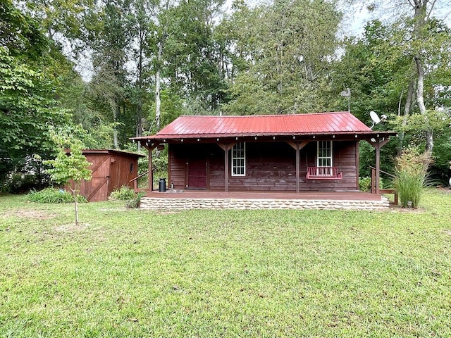 back of house with a lawn, a storage unit, metal roof, and a porch