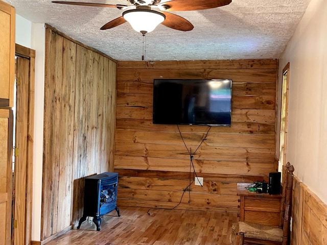 living room with a textured ceiling, a wood stove, ceiling fan, wooden walls, and wood finished floors