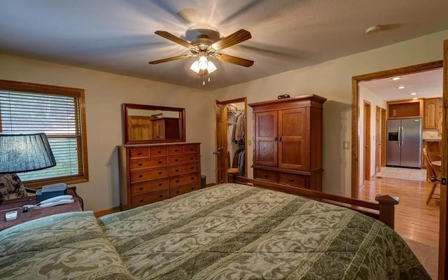 bedroom featuring stainless steel fridge with ice dispenser, a walk in closet, light hardwood / wood-style floors, and ceiling fan