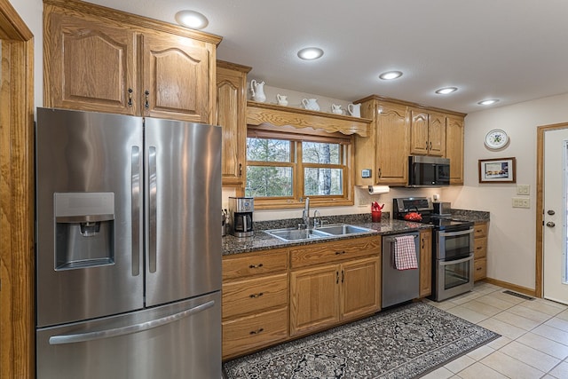 kitchen featuring stainless steel appliances, dark stone countertops, sink, and light tile patterned floors