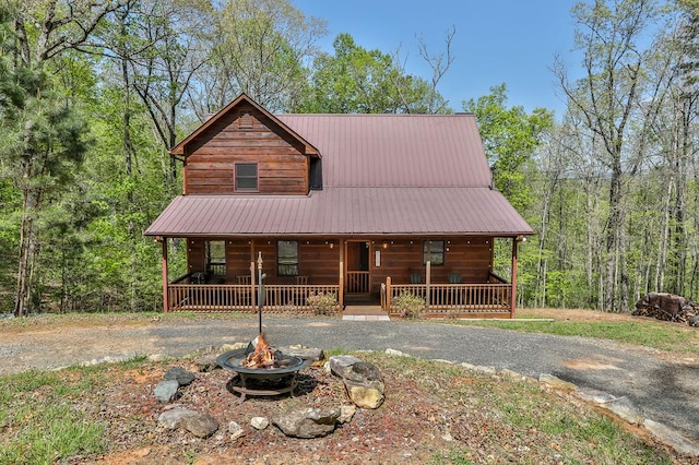 view of front of house featuring a wooded view, a fire pit, covered porch, and driveway