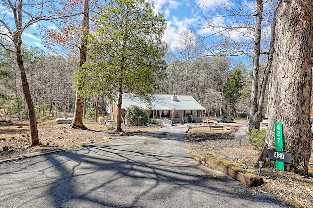 view of front of home featuring a view of trees, a porch, and driveway