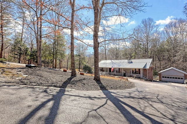 view of front facade with covered porch, an outdoor structure, a detached garage, brick siding, and metal roof