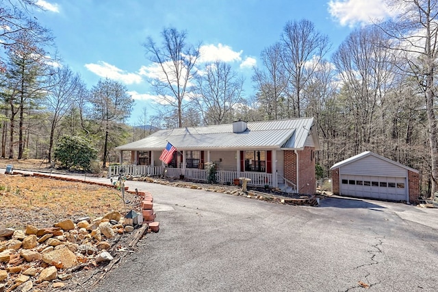 view of front facade with an outbuilding, a detached garage, a porch, metal roof, and brick siding