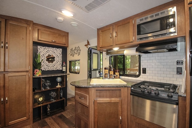 kitchen featuring decorative backsplash, dark stone counters, dark hardwood / wood-style floors, sink, and stainless steel appliances