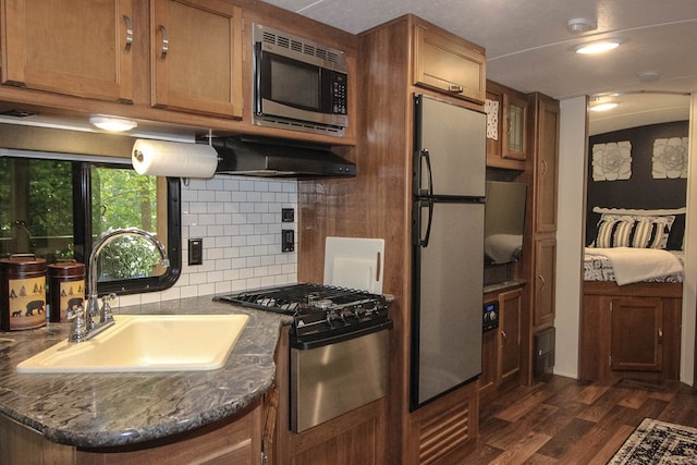 kitchen with dark hardwood / wood-style floors, stainless steel appliances, dark stone countertops, sink, and tasteful backsplash