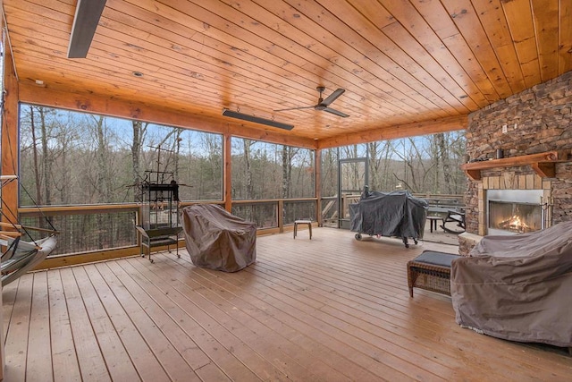 sunroom / solarium with a wealth of natural light, ceiling fan, wood ceiling, and an outdoor stone fireplace