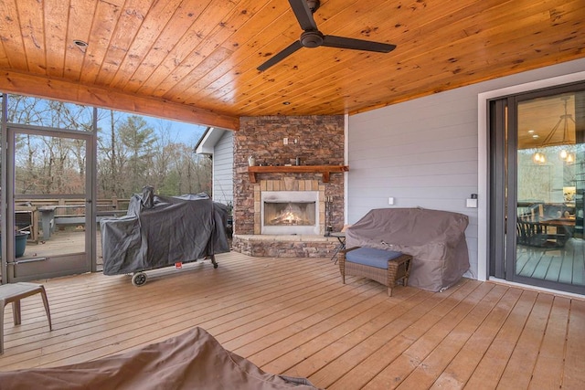 wooden deck featuring area for grilling, a stone fireplace, and ceiling fan