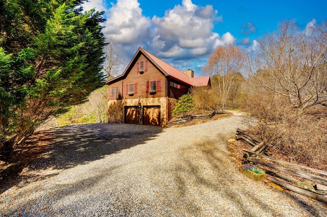 view of side of home with an attached garage, driveway, a chimney, and stone siding