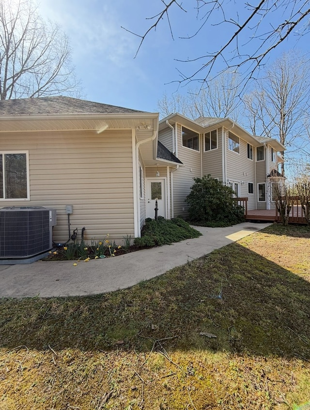 view of side of property with a wooden deck, central AC unit, and a lawn