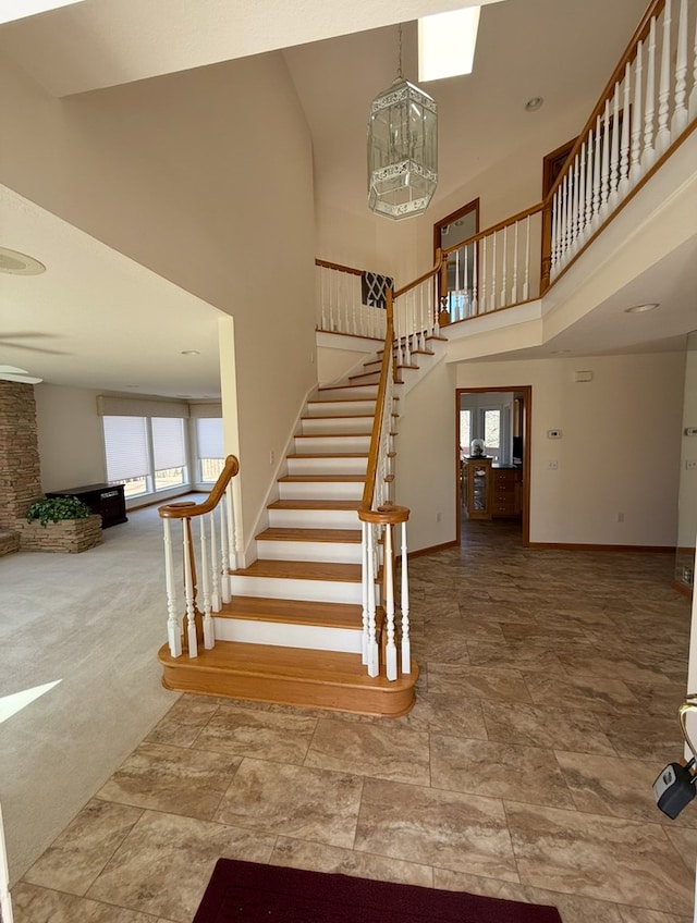 stairs featuring carpet floors, baseboards, a towering ceiling, and stone finish flooring