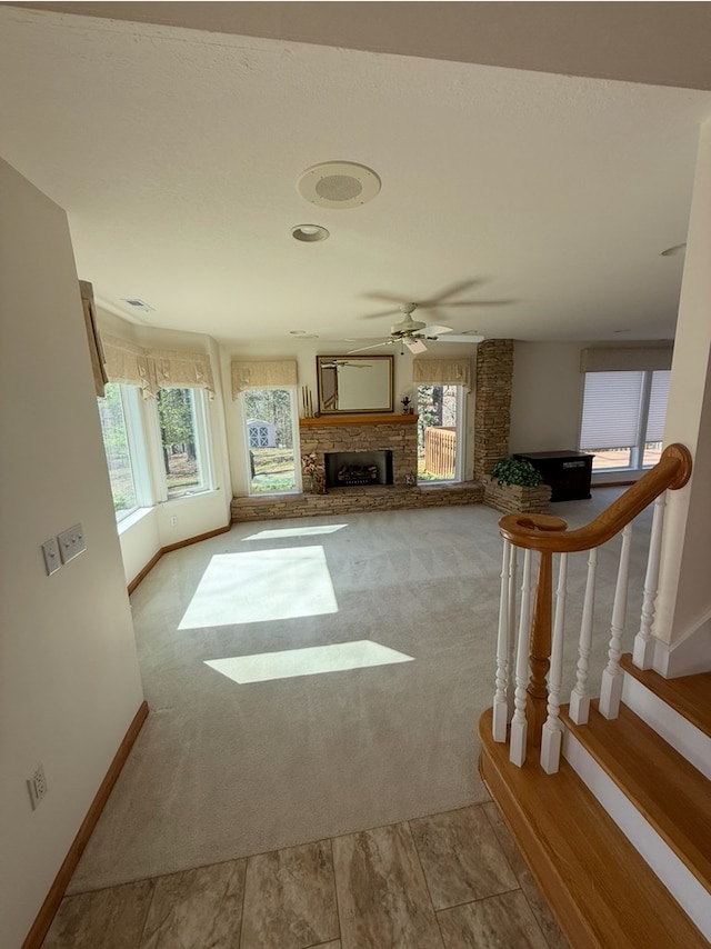 unfurnished living room featuring carpet floors, a ceiling fan, a stone fireplace, and a wealth of natural light