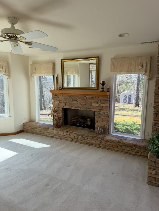 unfurnished living room with visible vents, baseboards, a stone fireplace, a ceiling fan, and carpet