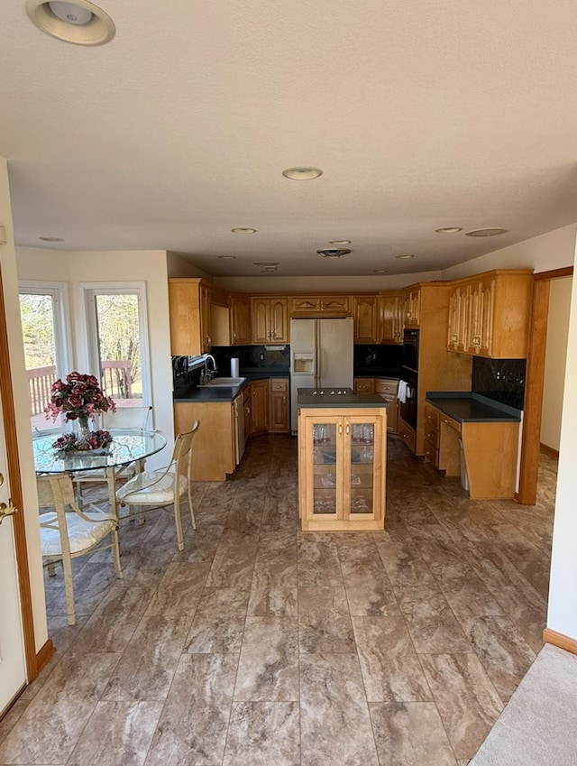 kitchen featuring white refrigerator with ice dispenser, a center island, a sink, black oven, and dark countertops