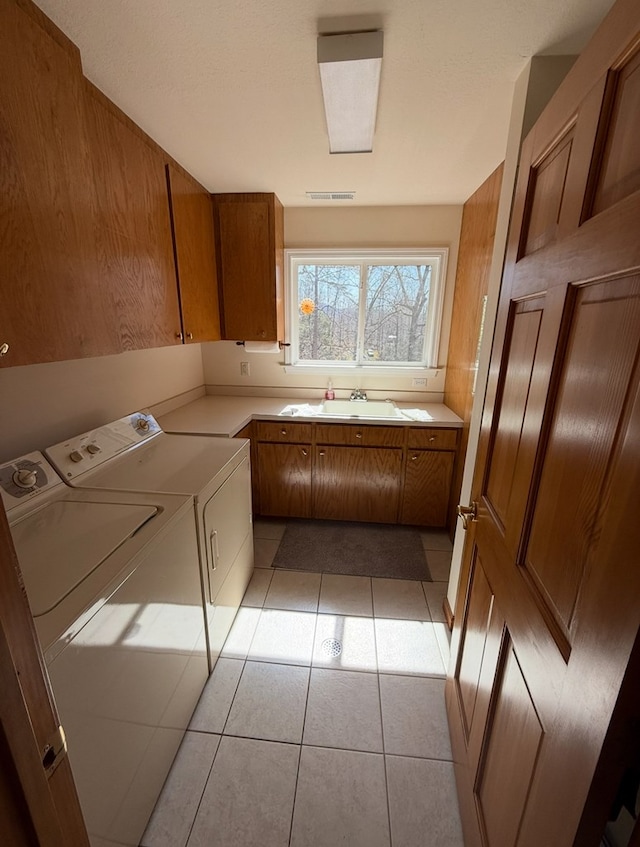 laundry area featuring visible vents, a sink, cabinet space, washing machine and clothes dryer, and light tile patterned flooring