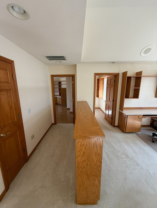 hall with light carpet, baseboards, and visible vents