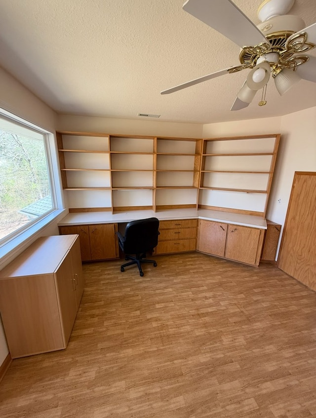 unfurnished office featuring light wood-type flooring, a ceiling fan, visible vents, and a textured ceiling