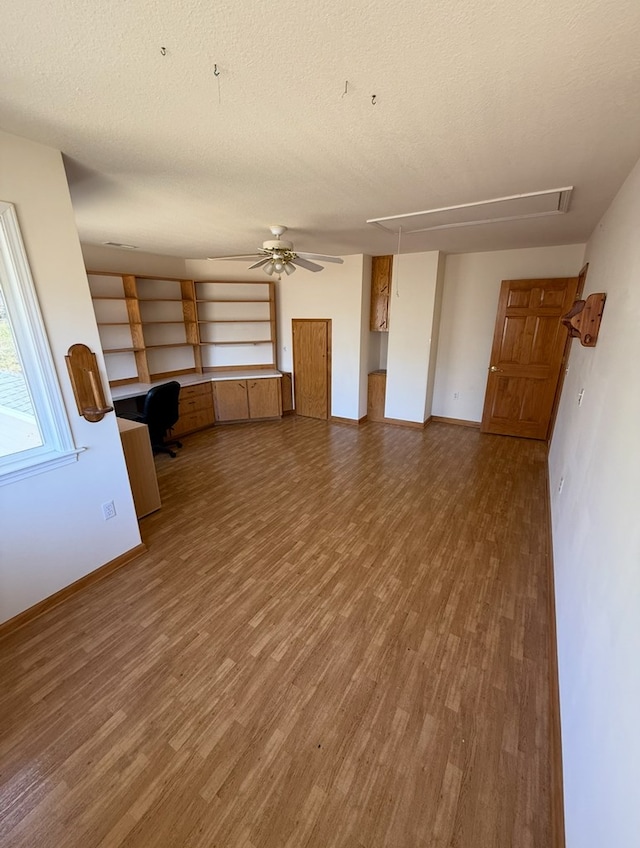 unfurnished living room with baseboards, attic access, wood finished floors, and a textured ceiling