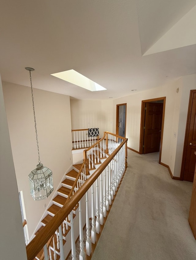 hall with a skylight, light colored carpet, baseboards, and an upstairs landing