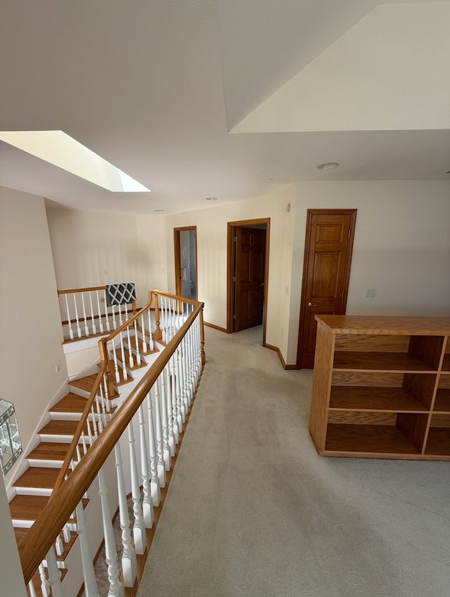 hallway featuring an upstairs landing, light colored carpet, baseboards, and a skylight