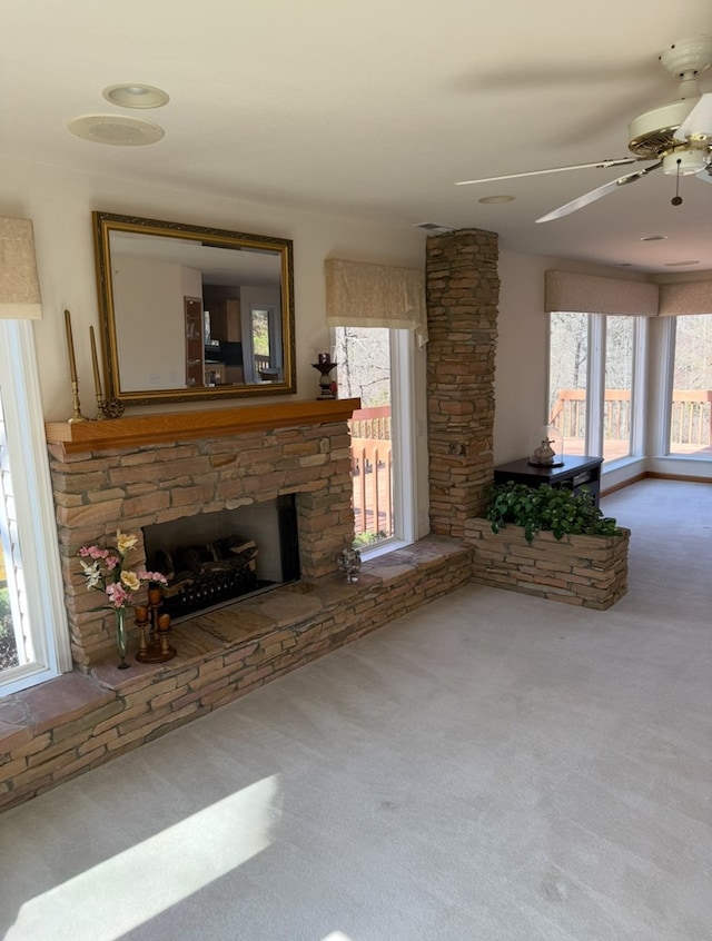 unfurnished living room featuring a ceiling fan, a stone fireplace, and carpet