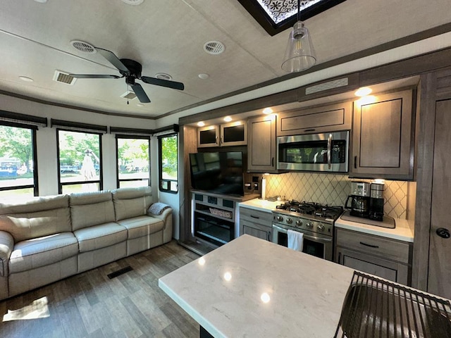 kitchen featuring stainless steel appliances, crown molding, ceiling fan, dark wood-type flooring, and backsplash