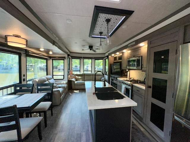 kitchen featuring stainless steel appliances, an island with sink, backsplash, ceiling fan, and sink