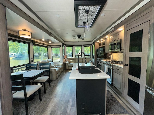 kitchen with ceiling fan, decorative backsplash, a wealth of natural light, a center island with sink, and appliances with stainless steel finishes