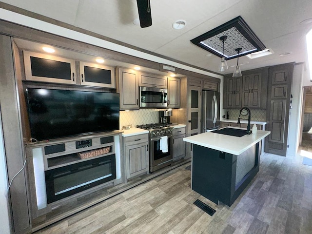 kitchen featuring an island with sink, appliances with stainless steel finishes, backsplash, and hardwood / wood-style floors