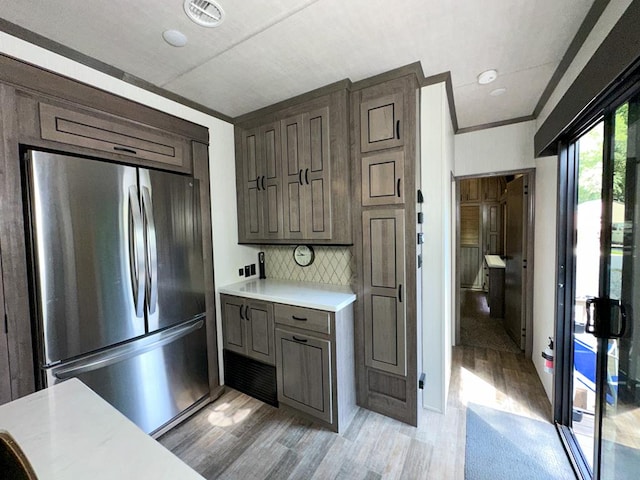 kitchen featuring decorative backsplash, crown molding, light hardwood / wood-style flooring, and stainless steel fridge