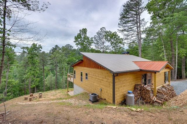 view of side of property featuring metal roof, a wooded view, and central AC unit