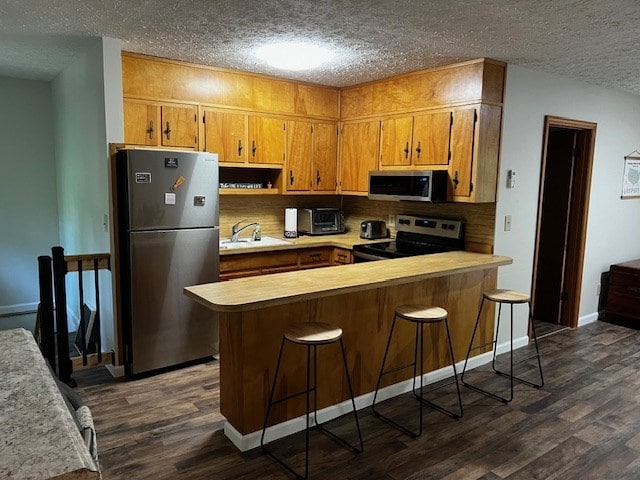 kitchen featuring appliances with stainless steel finishes, dark hardwood / wood-style floors, sink, a kitchen breakfast bar, and kitchen peninsula