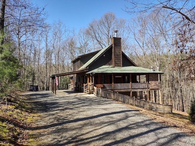 view of side of property featuring driveway, a chimney, and a porch