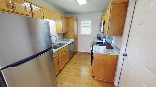 kitchen with light wood-type flooring, light stone counters, stainless steel appliances, and sink