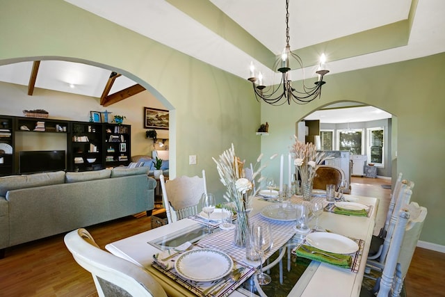 dining area featuring a chandelier, wood-type flooring, and lofted ceiling with beams