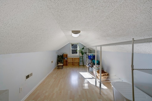 additional living space featuring a textured ceiling, light hardwood / wood-style floors, and lofted ceiling