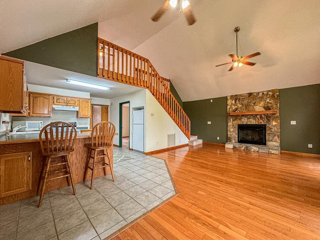 kitchen featuring a fireplace, light hardwood / wood-style flooring, a breakfast bar, high vaulted ceiling, and ceiling fan