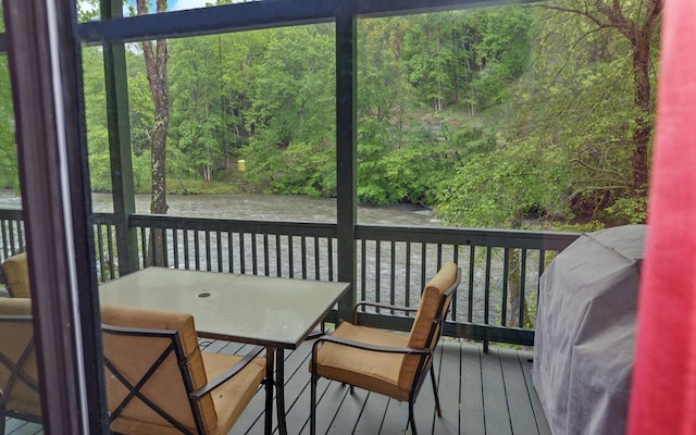 deck with outdoor dining space, a wooded view, and a water view