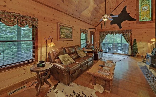 living area featuring a wood stove, wood walls, wood finished floors, a ceiling fan, and lofted ceiling