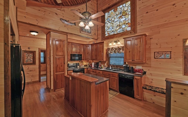 kitchen featuring black appliances, wooden walls, a sink, light wood finished floors, and dark countertops