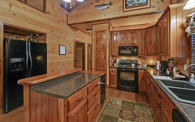 kitchen with black appliances, a sink, wooden walls, brown cabinets, and light wood-style flooring